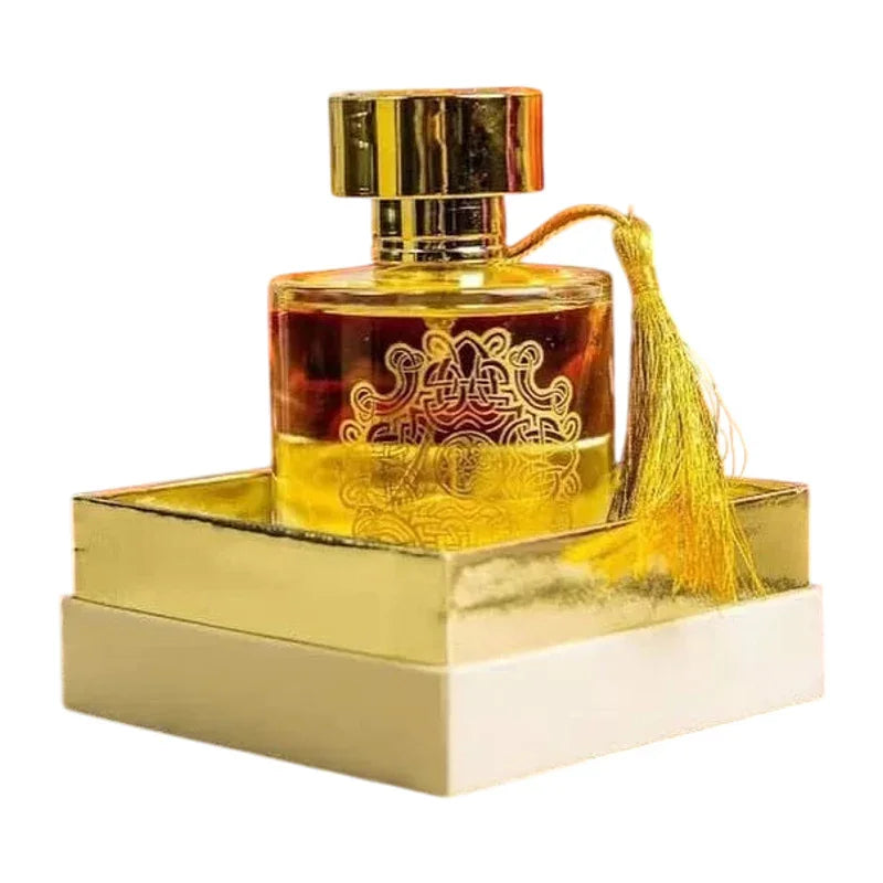 Flacon de parfum doré avec pomme à pulvériser et pompon décoratif sur un socle blanc